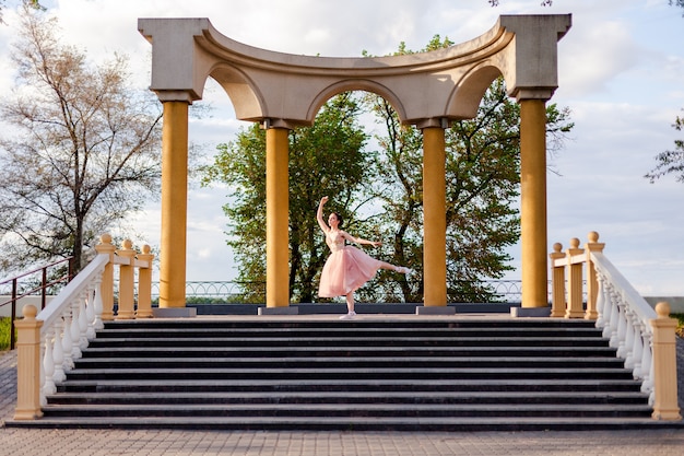 Una bailarina baila con la pierna levantada en un arco de columnas en la arquitectura urbana en el terraplén ...