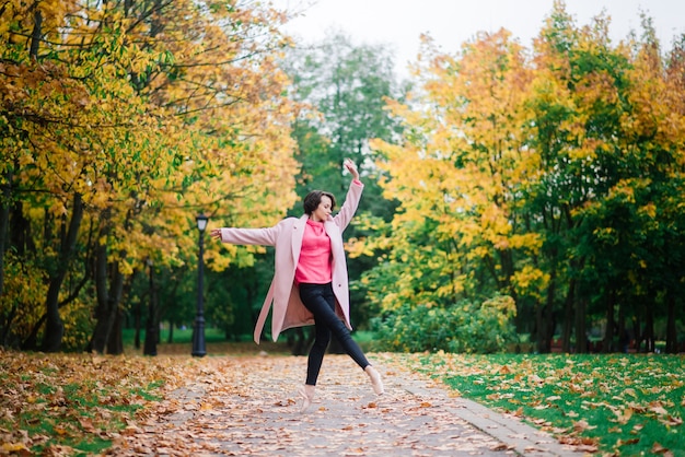 Bailarina bailando en la naturaleza entre hojas de otoño en abrigo justo.