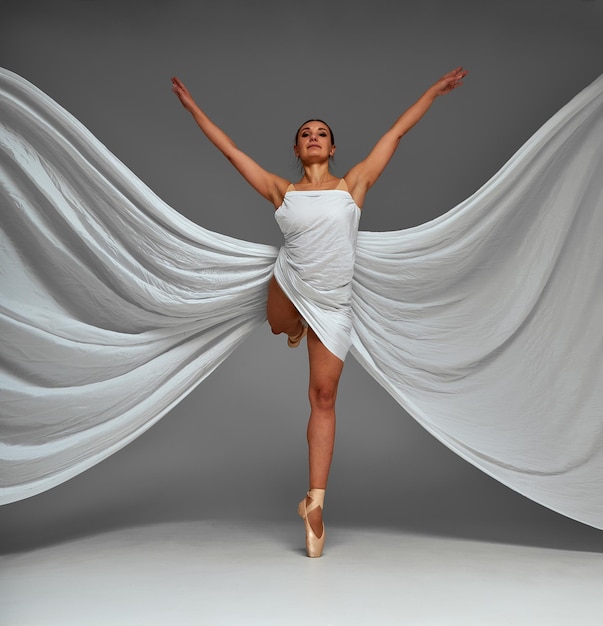 Bailarina bailando con tela de seda, bailarina de ballet moderna en tela ondulante, zapatos de punta, fondo gris.