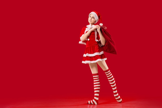 Bailarina bailarina con zapatos de punta con un regalo en las manos vestida como Santa Claus con un fondo rojo