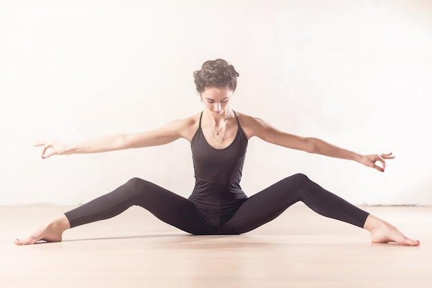 Bailarina de ballet joven delgada haciendo ejercicio de estiramiento sentado con las piernas bien separadas en el interior.
