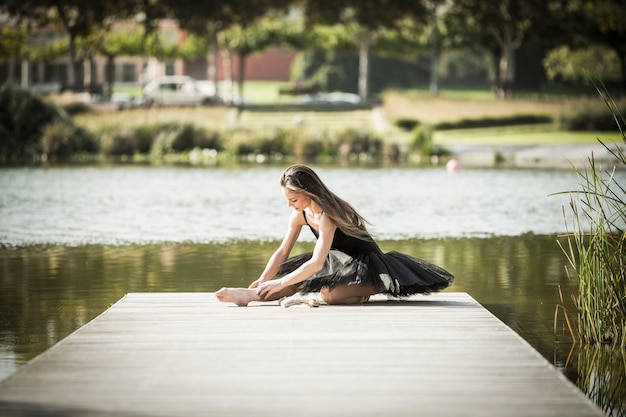 Foto bailarina clássica posando em uma passarela de um lago urbano em um dia ensolarado