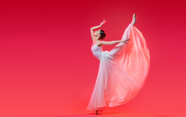 Bailarina elegante em sapatilhas dançando em uma longa saia branca em um fundo vermelho