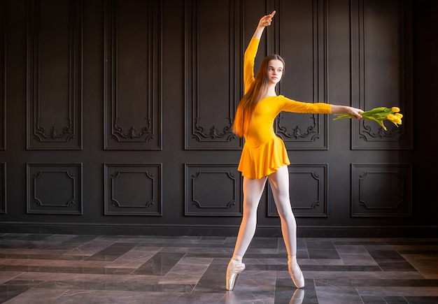 Bailarina elegante em sapatilhas de ponta dançando com um buquê de tulipas em um fundo cinza escuro