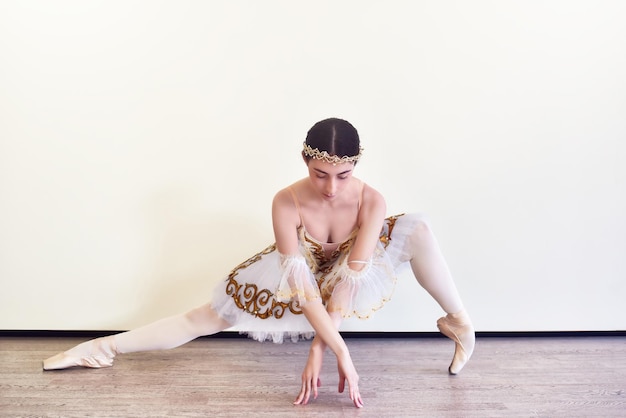 Bailarina elegante en tutú blanco practicando posiciones de ballet en el estudio