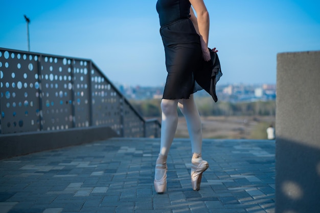 Bailarina em pernas de balé em sapatos e tutu preto dançando perto da cerca Linda jovem de vestido preto e ponta dançando do lado de fora Linda bailarina realizando uma dança ao ar livre Close-up