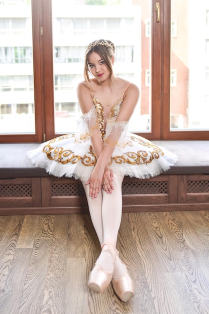 Bailarina em um tutu branco elegante senta-se e posa no peitoril da janela