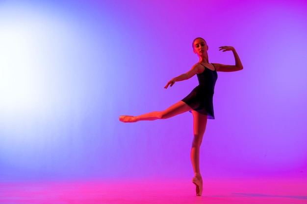 Bailarina hermosa joven en zapatillas de punta y silueta de leotardo rosa sobre fondo azul brillante.