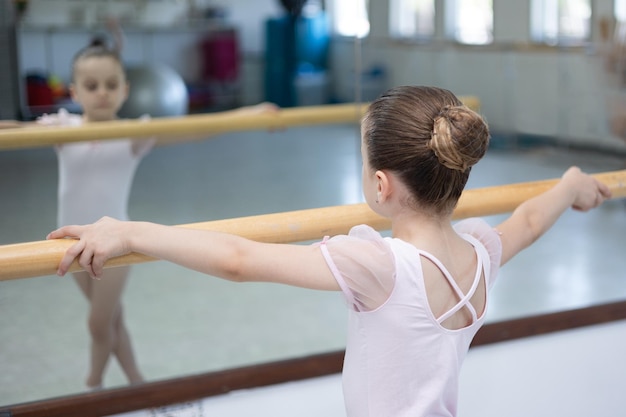 Bailarina infantil menina bonitinha em tutu rosa pálido e sapatilhas praticando movimentos de dança.