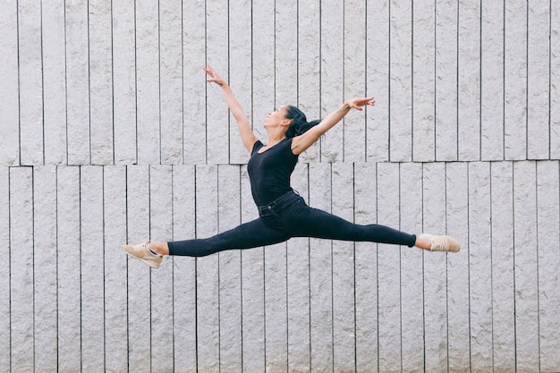 Bailarina interracial saltando aislado en una pared gris