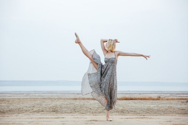 Bailarina joven agraciada en vestido hermoso bailando en la playa