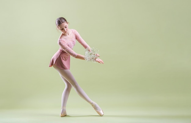 Bailarina joven elegante en zapatos de punta bailando sobre un fondo verde suave