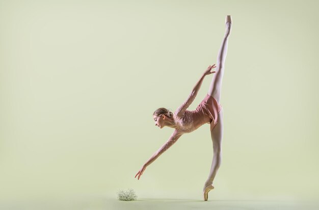 Bailarina joven elegante en zapatos de punta bailando sobre un fondo verde suave
