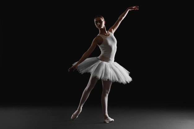 Bailarina joven practicando movimientos de baile sobre fondo negro