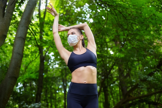 Una bailarina con máscara y zapatos de punta está haciendo ejercicios en un camino de madera en un parque forestal. concepto de entrenamiento al aire libre seguro