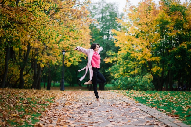 Bailarina de mujer bailando en zapatos de punta en el parque de otoño dorado, de pie en pose de ballet sobre hojas amarillas
