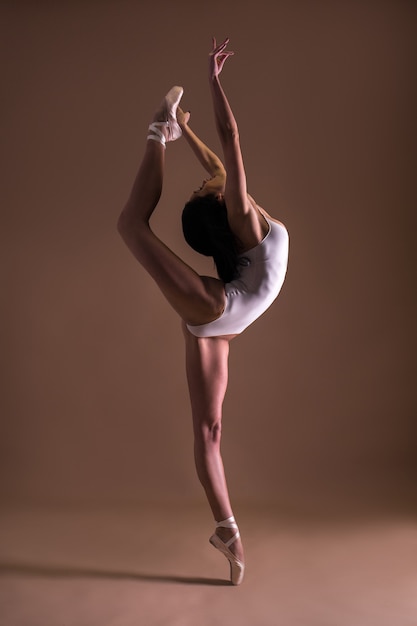 Bailarina de mujer hermosa joven posando en estudio sobre fondo beige