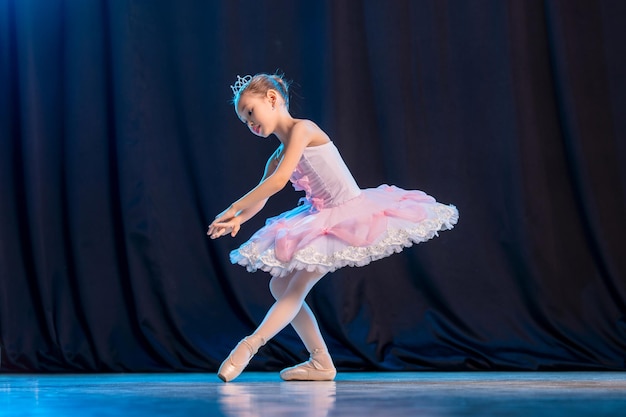 La bailarina de la niña está bailando en el escenario en tutú blanco en la variación clásica de los zapatos de punta.