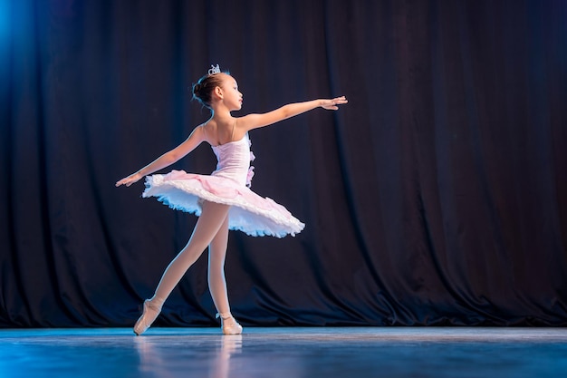 Bailarina de niña está bailando en el escenario en tutú blanco en variación clásica de zapatos de punta.