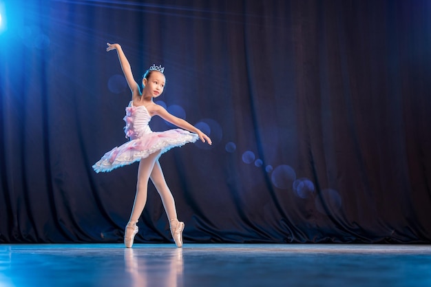 Bailarina de niña está bailando en el escenario en tutú blanco en variación clásica de zapatos de punta.