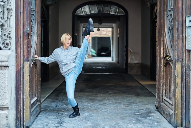 Bailarina profesional levantando su pierna y el otro pie de puntillas, apoyado en una puerta de madera de un edificio. Danza urbana