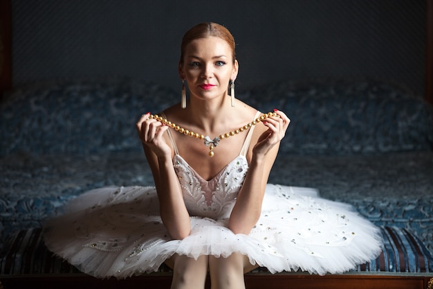 Bailarina sentada en la cama con collar de perlas