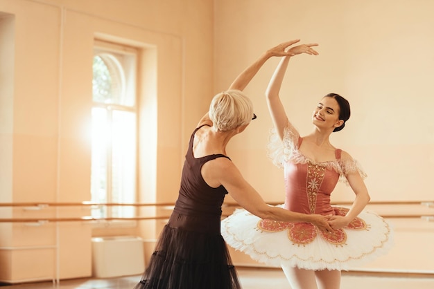 Bailarina sonriente bailando mientras la maestra la ayuda en el estudio de ballet