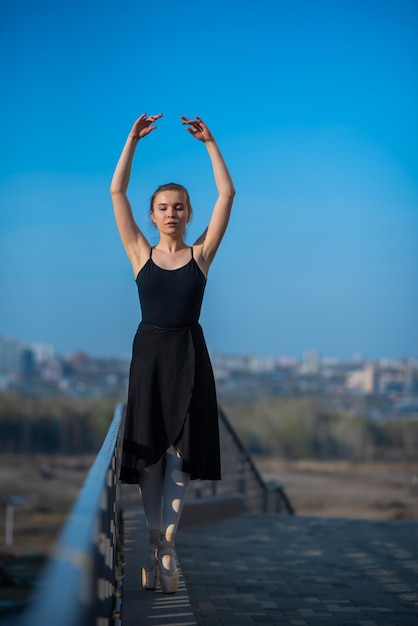 Bailarina en un tutú posando cerca de la valla Hermosa mujer joven en vestido negro y baile de punta afuera Hermosa bailarina demuestra un estiramiento increíble