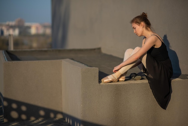 Bailarina en un tutú posando cerca de la valla Hermosa mujer joven con un vestido negro y zapatos de punta afuera Hermosa bailarina demuestra un increíble estiramiento