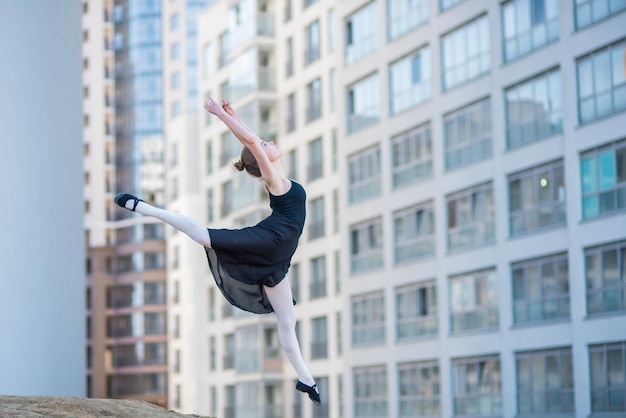 Bailarina en tutú posando contra un edificio residencial Hermosa mujer joven en vestido negro y zapatillas de punta saltando con increíble flexibilidad Bailarina realiza saltos elegantes con desviación