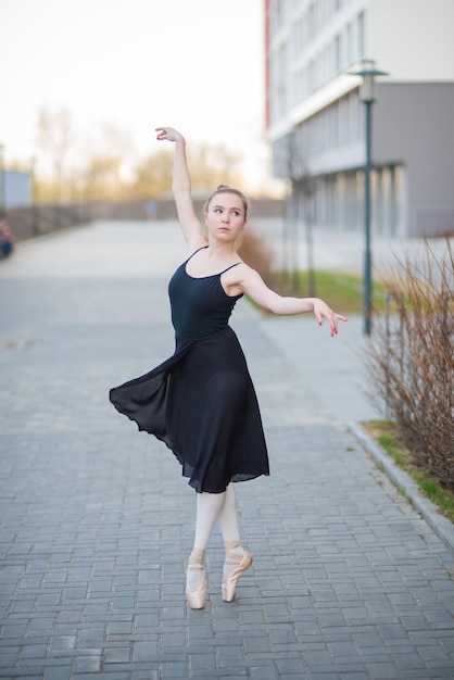 Bailarina en un tutú posando contra el telón de fondo de un edificio residencial Hermosa mujer joven en vestido negro y zapatos de punta bailando ballet fuera Elegante danza clásica