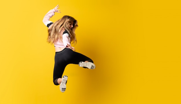 Foto bailarina urbana bailando sobre fondo amarillo aislado y saltando