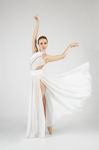 Foto una bailarina con un vestido blanco y zapatos de punta se para en sus dedos de los pies y baila sobre un fondo blanco