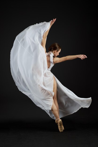 Foto una bailarina con un vestido blanco y zapatos de punta se para en sus dedos de los pies y baila sobre un fondo negro