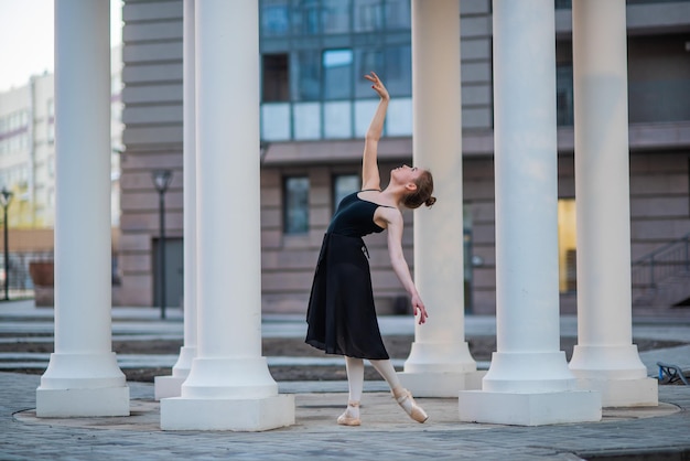 Bailarina con un vestido negro es una pose hermosa Una hermosa joven con un traje negro baila en una elegante danza clásica sobre un fondo de columnas