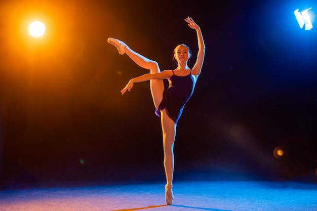 Bailarina con un vestido negro está bailando iluminada por haces multicolores de focos