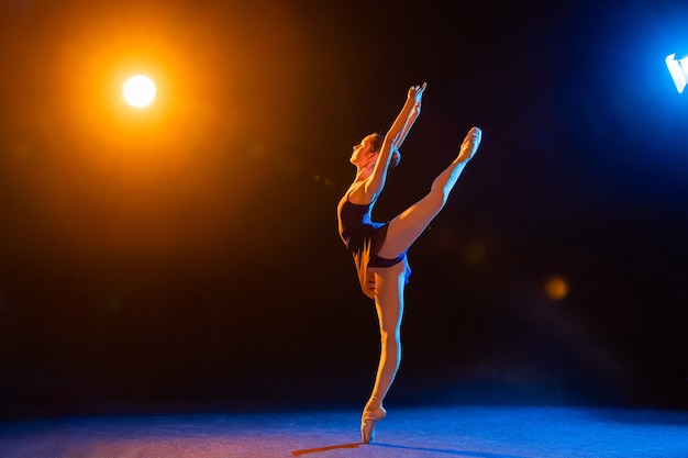 Bailarina con un vestido negro está bailando iluminada por haces multicolores de focos