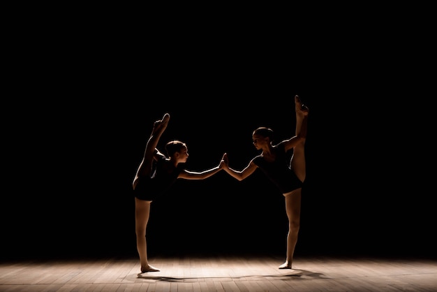 Bailarinas flexibles estiran en una escena iluminada oscura