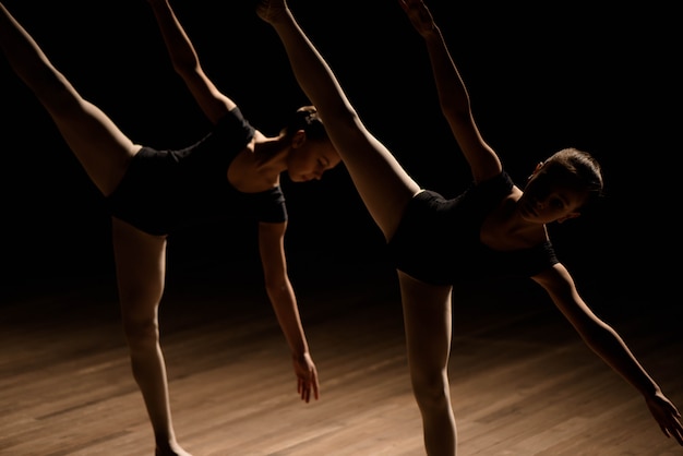 Bailarinas flexíveis esticar em uma cena escura iluminada