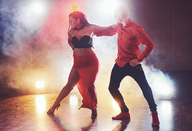 Foto bailarines hábiles actuando en la habitación oscura bajo la luz y el humo del concierto una pareja sensual realizando una danza contemporánea artística y emocional