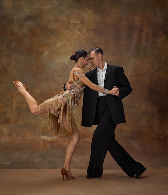 Bailarines de tango profesionales de hombre y mujer con hermosos y elegantes trajes de escenario actuando sobre un fondo vintage oscuro