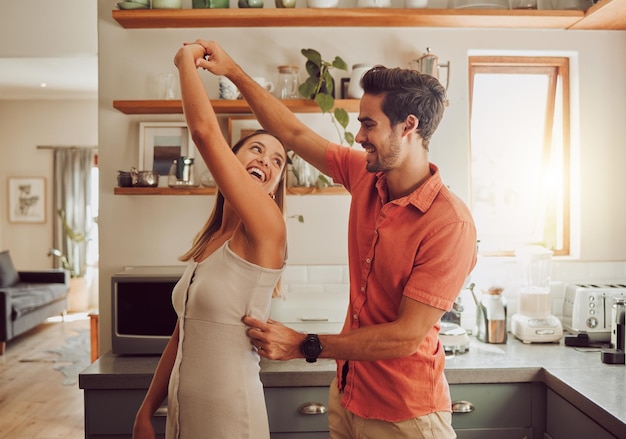 Baile alegre y pareja amorosa uniéndose y divirtiéndose en la cocina juntos en casa Diversión enérgica y relación activa compartiendo un baile y un momento romántico mientras disfrutan de su aniversario