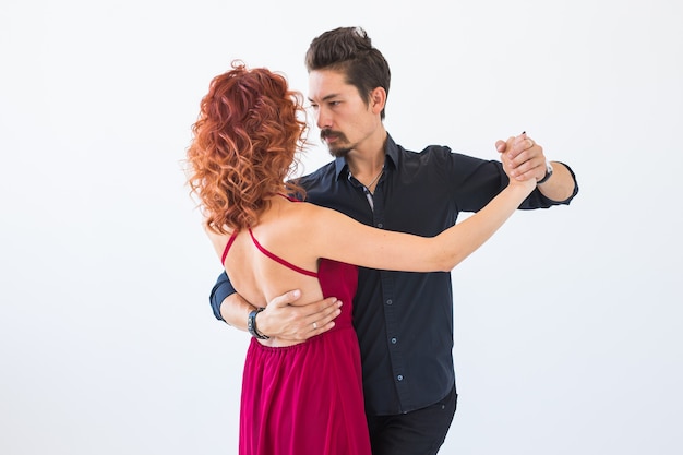 Foto baile social, bachata, kizomba, salsa, concepto de tango - mujer vestida con vestido rojo y hombre con traje negro sobre pared blanca.