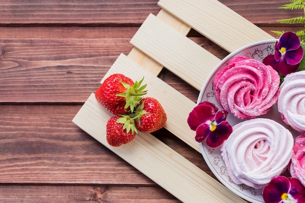 Baiser. Das Konzept der Feier. Valentinstag Geschenk. Selektiver Fokus, Kopienraum-Eibisch, flaumiger Nachtischzefir, rosa Strudelmeringe und Erdbeere.