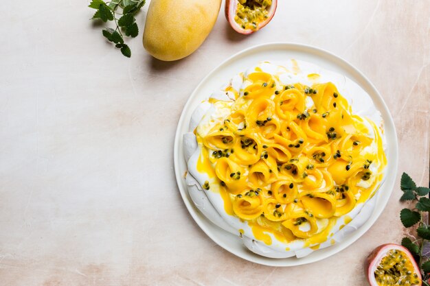 Baiserkuchen Pavlova mit frischer Mango und Maracuja und Schlagsahne auf Schiefer-, Stein- oder Betonhintergrund, Draufsicht