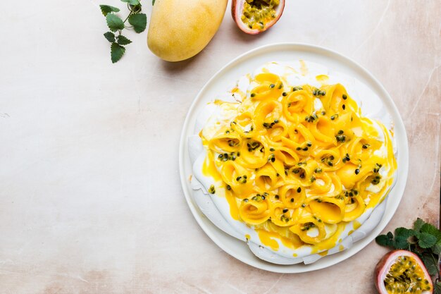 Baiserkuchen Pavlova mit frischer Mango und Maracuja und Schlagsahne auf Schiefer-, Stein- oder Betonhintergrund, Draufsicht