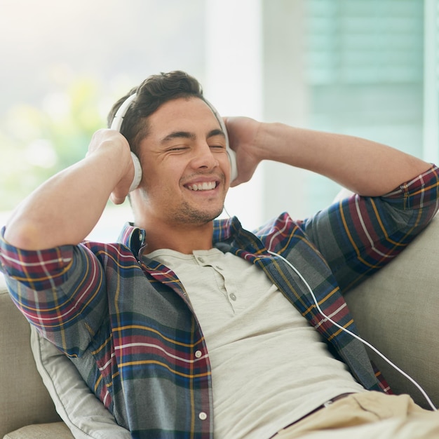 Baja la semana, sube la música Foto de un joven relajándose en el sofá y escuchando música con auriculares en casa