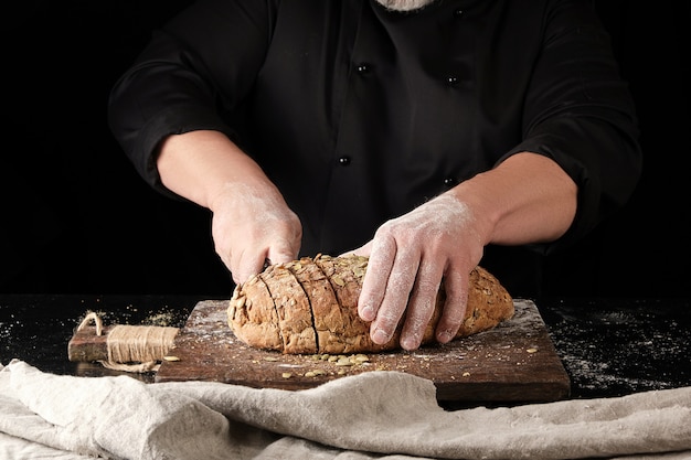 Baker de uniforme preto corta uma faca em fatias de pão de centeio