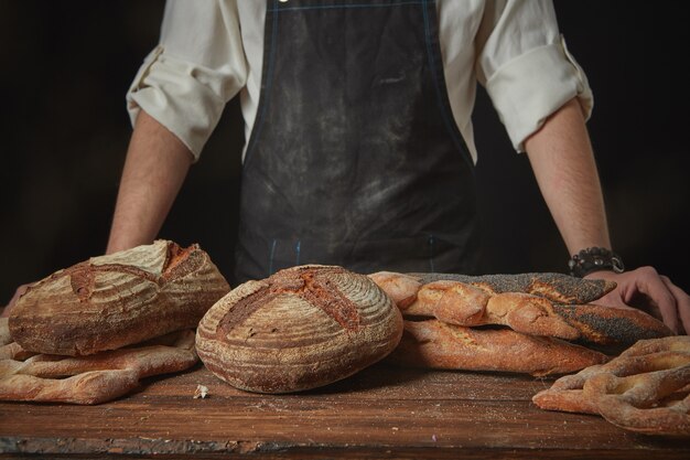 Baker en un delantal con pan recién hecho sobre una mesa de madera marrón