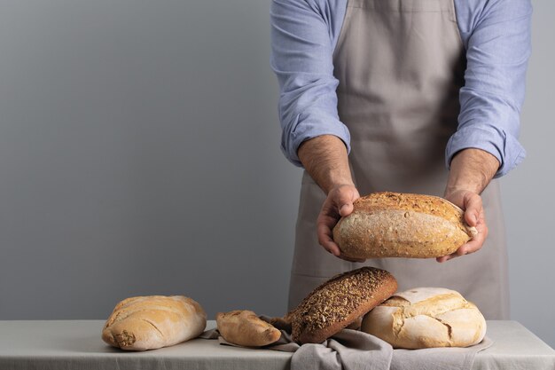 Baker segurando pão fresco sobre a mesa em fundo cinza